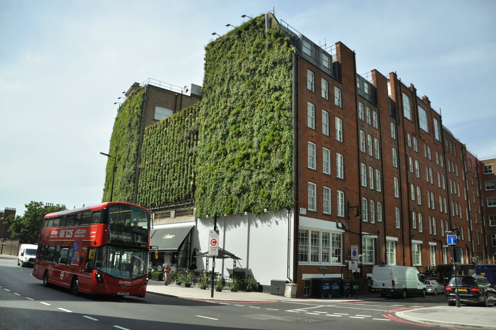 Green façade covering a red brick Mayfair building above a London street with a red bus passing